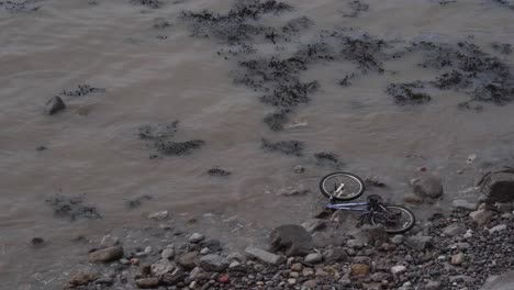 bicycle abandoned in the beach, waves crushing into a bike that was trowed into the sea, see weeds floating and crushing in the beach