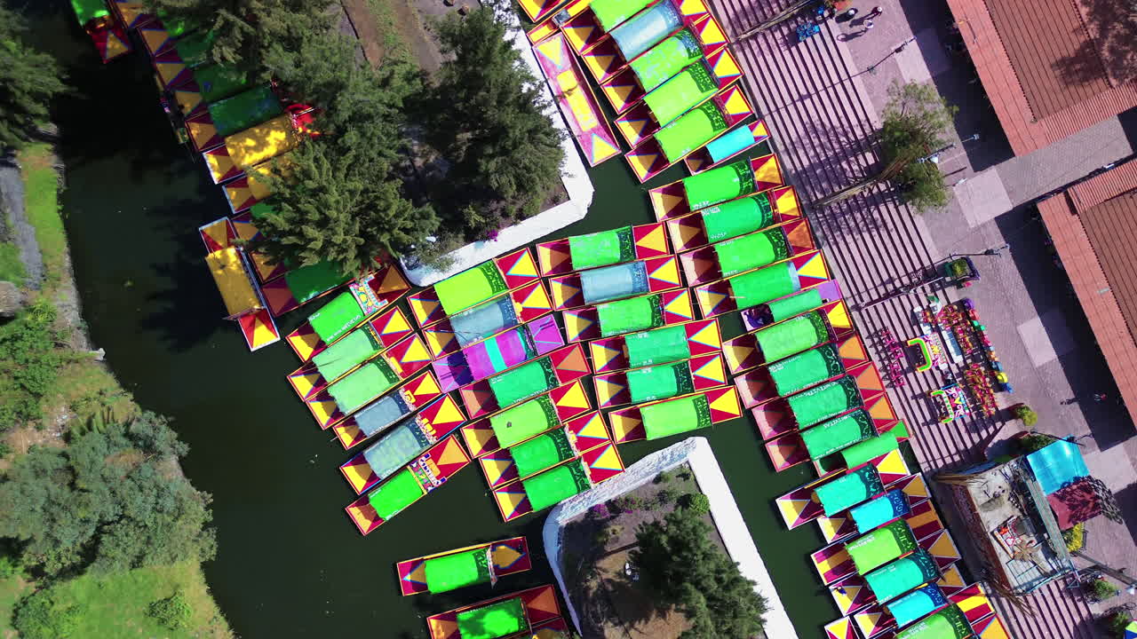 Colorful gondolas floating along Xochimilco famous canals in Mexico City, a cultural UNESCO site, top down orbit at dock