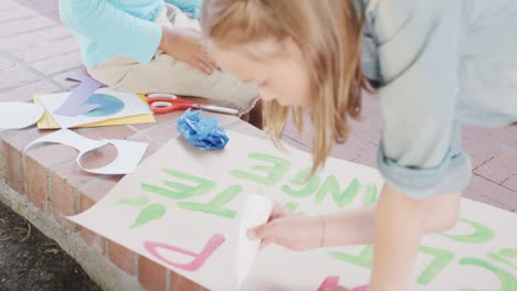 video of caucasian schoolgirl making protest placard in schoolyard, copy space