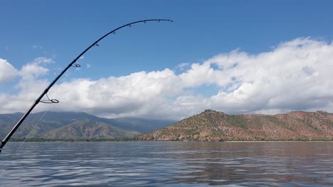 una caña de pescar con línea de arrastre para pescar en un vasto océano tranquilo en un perfecto día de verano soleado y azul cielo con tierra visible en la distancia