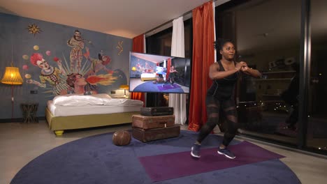 african-american woman doing some steps exercise inside her bedroom in a condominium overlooking a city below