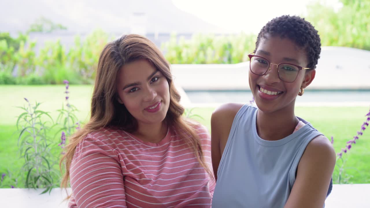 Amigas diversas sentadas num banco branco na varanda, a posar para a câmara, a abraçar-se e de mãos dadas.
