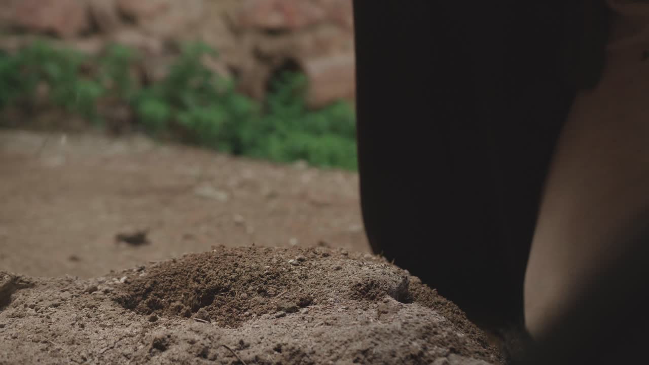 Close-up of a hand in a leather bracer digging soil with an ancient pickaxe. Historical reenactment or fantasy scene of hard labor, excavation, or searching for treasure