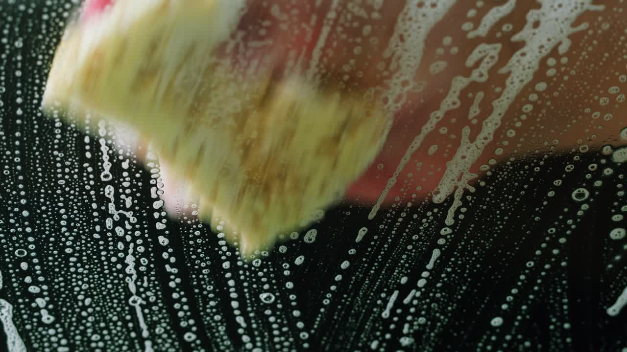 Close-Up of Hand Washing Glass Surface with Sponge and Soap Suds