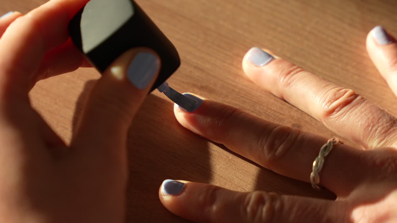 Female hand applying blue nail polish. Close-up of home beauty routine
