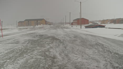 snow drifted by the wind blows over the vast streets of longyearbyen during a storm, away from the camera into the distance