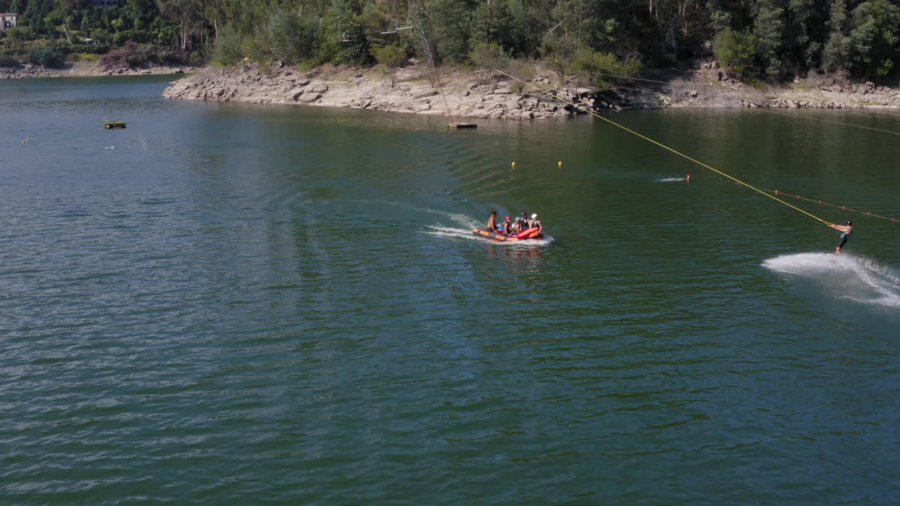Uomo che fa wakeboard con persone che vanno in barca sul lago calmo dell'Isola di Ermal, Portogallo, durante le vacanze estive.