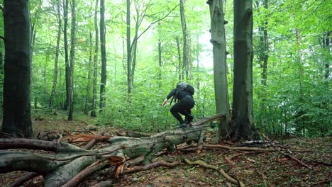 hombre con una mochila sube sobre un árbol caído en cámara lenta en un frío día de otoño en el bosque