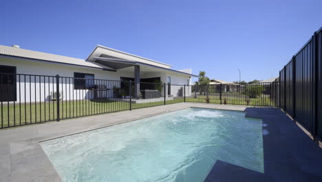 outdoor entertainment area, marble tiles luxurious contemporary outdoor swimming pool in ground, clear blue water black fence grey tiled decking close up of pool spa modern home green grass blue skies