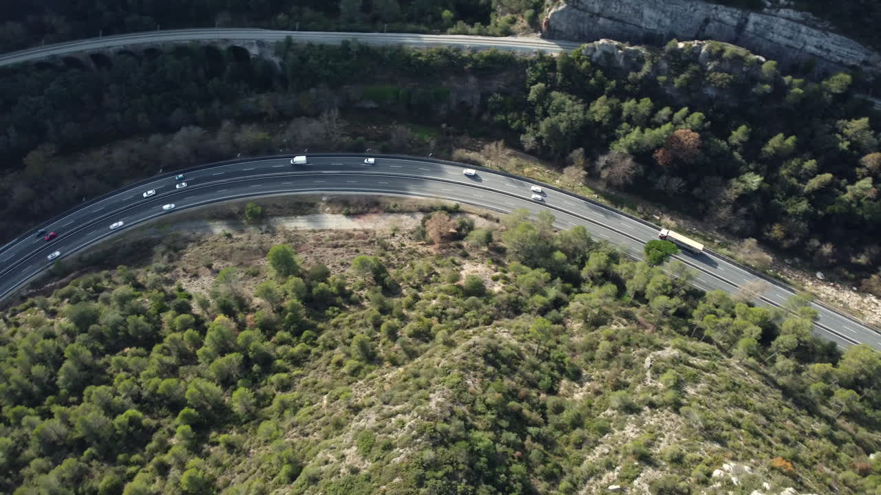 Aerial view of a highway winding through a mountain valley with a warehouse.
