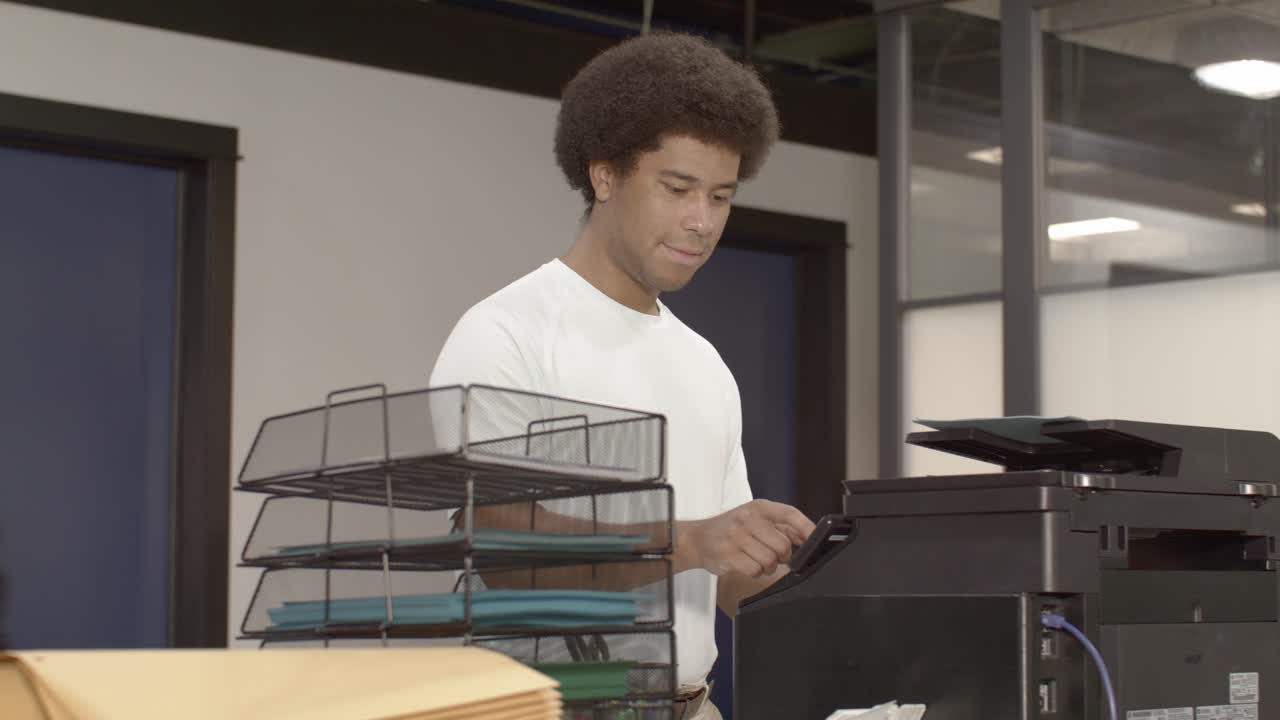 African American man at a printer in a busy office with video dolly right to left