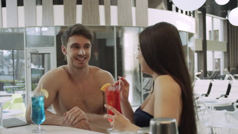 Beautiful-couple-chatting-in-spa.-Smiling-man-woman-drinking-cocktails-at-resort