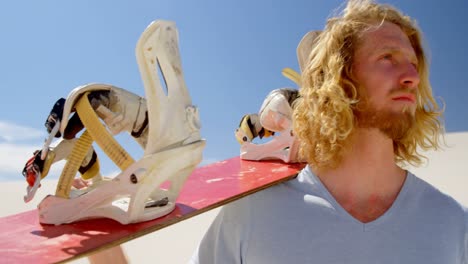 blonde man with sand board looking at a distance in desert 4k