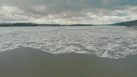 agua de río gris profundo con hielo blanco contra densos bosques