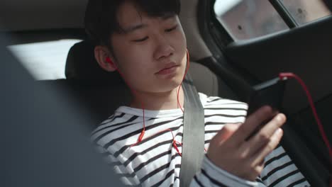 asian teenager listening to music on smartphone in car