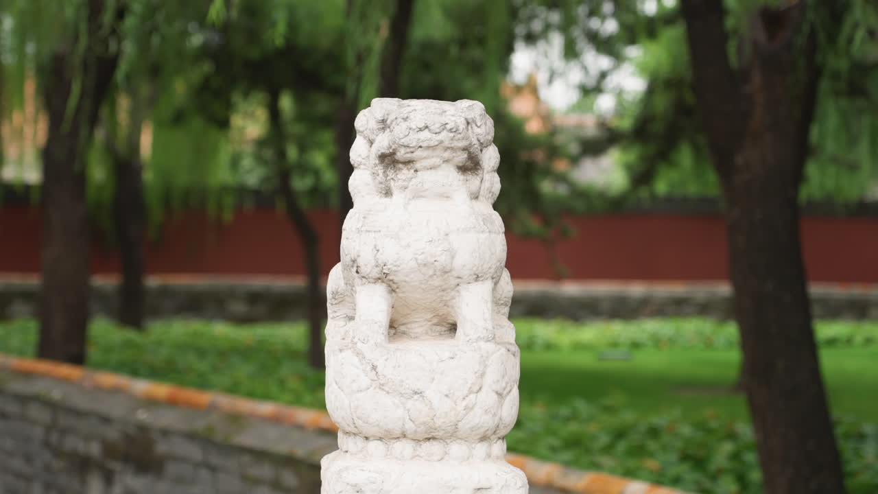 Leone guardiano di pietra in un giardino del tempio, statua bianca consumata dal tempo appollaiata su una balaustra di pietra, salici e muro rosso del cortile sfocati, sentiero in mattoni muschiosi e vegetazione rigogliosa, patrimonio sereno