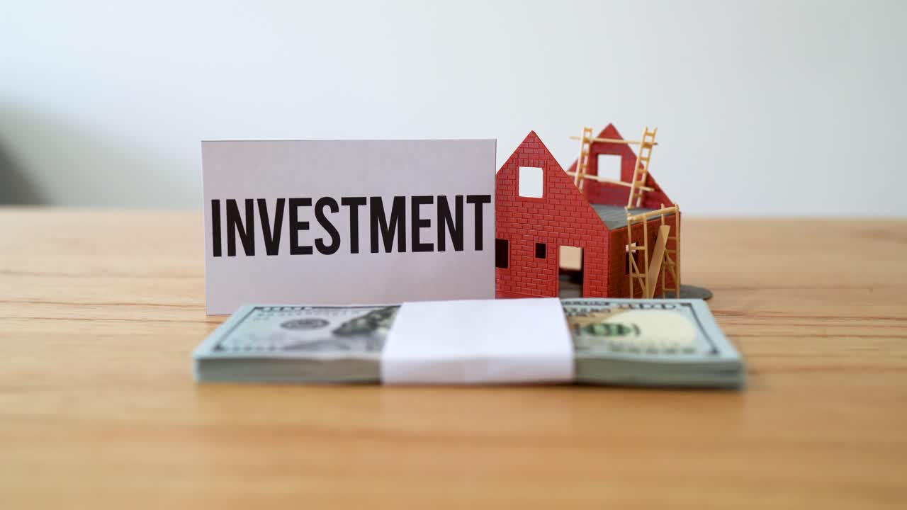 Concept of investing in real estate development projects. Pile of cash next to a house in construction.