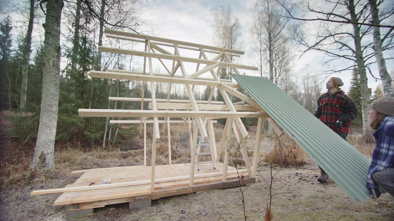 Svensk par monterer bølgeplade på trækonstruktionen af en off-grid hytte.
