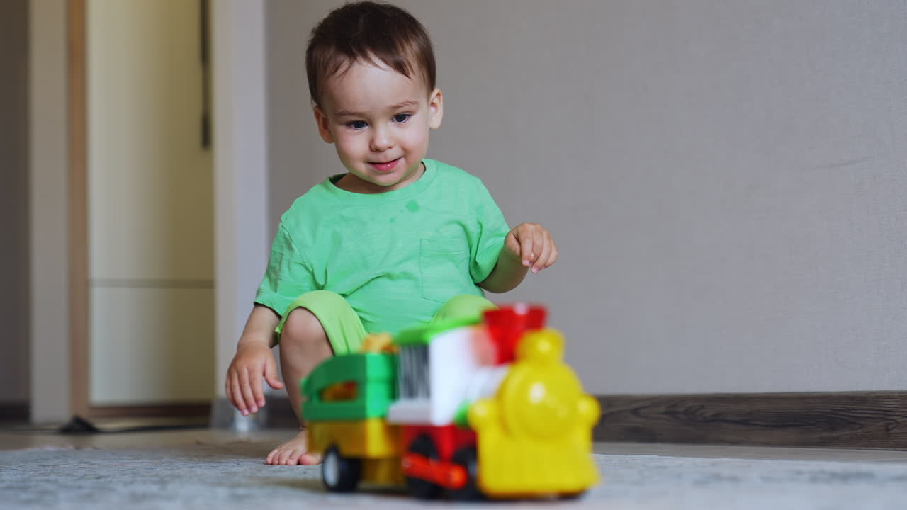 Adorable toddler boy squatted in the room. Little kid pushes his car and crawls after it excitedly.