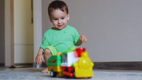 adorable toddler boy squatted in the room. little kid pushes his car and crawls after it excitedly.