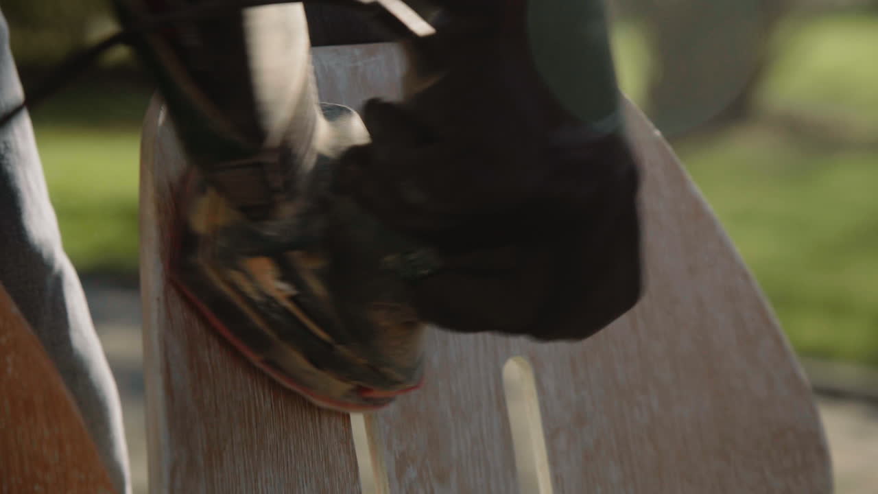 toma de detalle de las manos de un manitas que usa una máquina pulidora para pulir madera y restaurar una vieja silla de diseño vintage en el jardín en un día soleado 4k destello de lente