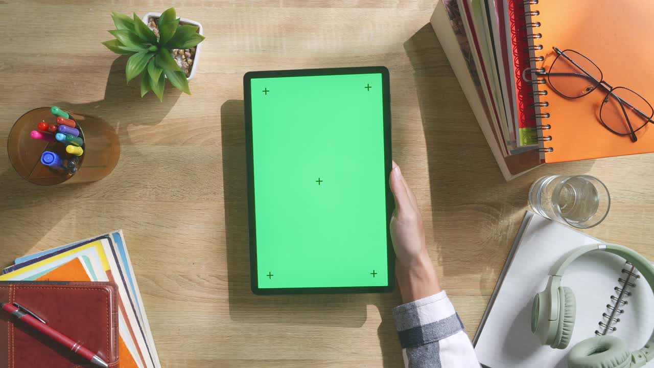 vista de arriba hacia abajo de una computadora portátil con pantalla verde simulada pantalla chromakey en un escritorio de oficina de madera al lado de la libreta con bolígrafos, gafas y un vaso de agua.