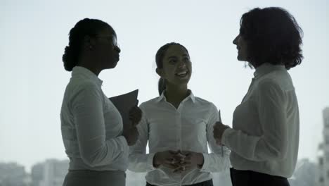 alegres mujeres de negocios multiétnicas estrechando la mano y hablando