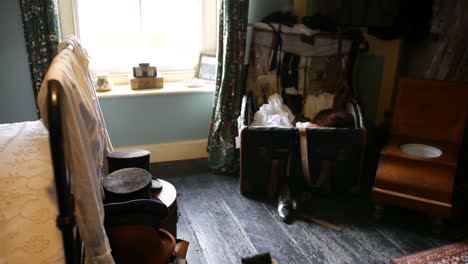 vintage room with old-fashioned luggage, wooden commode chair, and patterned textiles, evoking historical home life