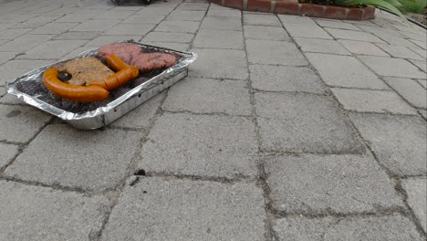 Locked-off-view-of-disposable-mini-BBQ-grill-with-different-meats-SLOW-MOTION