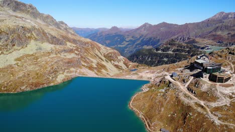 Bird's-Eye-View-Of-Berghotel-Rudolfshutte,-Weisssee-Glacier-Lake-And-Dam-On-A-Sunny-Day-In-Austria