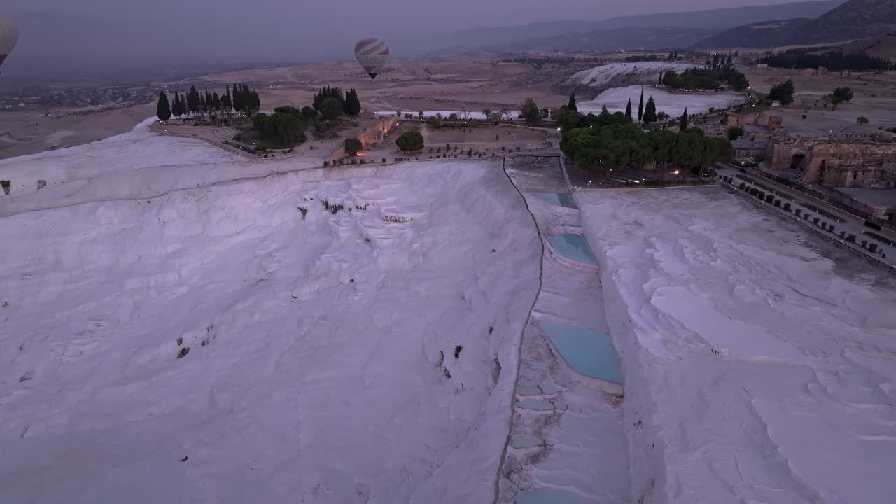 Aerial view of Pamukkale terraces under sunrise sky and rising balloons
