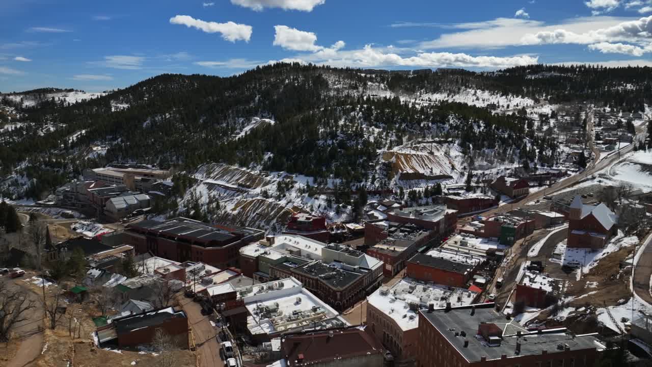 Snowy historic downtown Central City Blackhawk Casino's Idaho Springs sunny blue skies clouds winter day clouds aerial drone Colorado Gold mine Rocky Mountains buildings cars road Gilpin County pan