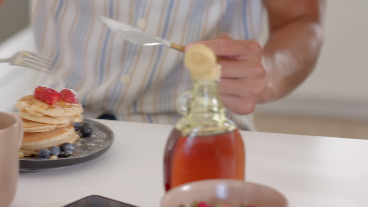 Sitting at breakfast table, person eating pancakes with fresh berries, at home