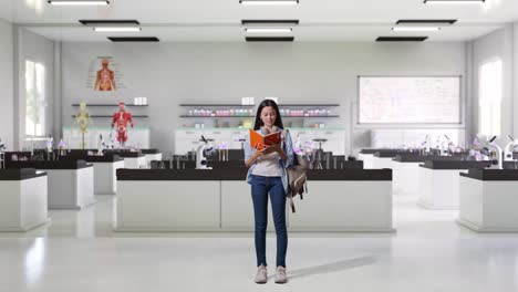 cuerpo lleno de estudiante adolescente asiática con una mochila sosteniendo y leyendo un libro mientras estaba de pie en el laboratorio de ciencias
