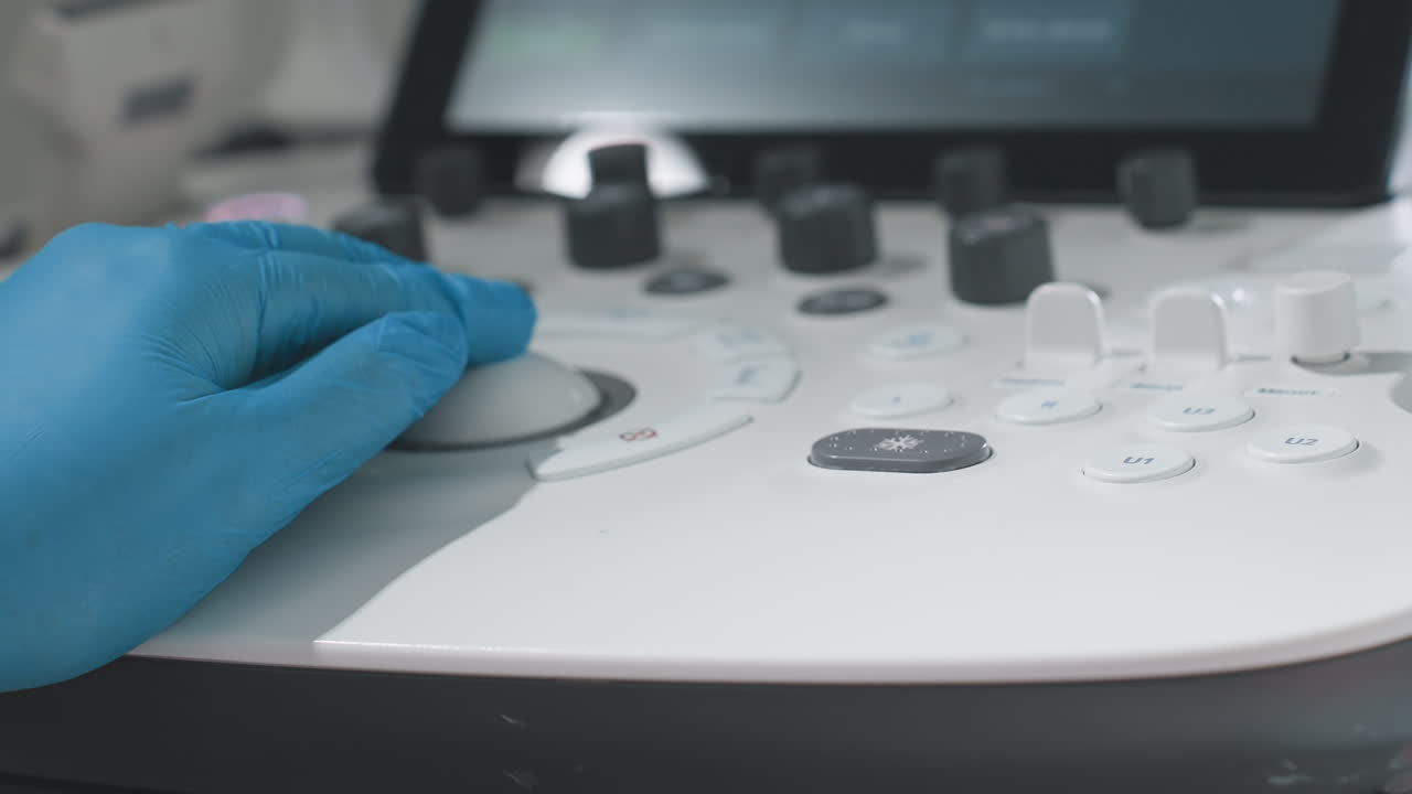 Lab technology specialist wearing sterile blue gloves carefully adjusts multiple control buttons on diagnostic machine during patient scan, demonstrating precision and focus in clinical examination