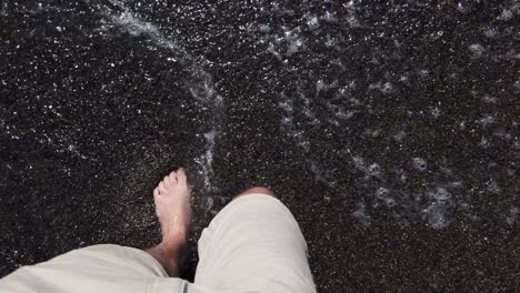 4k-video---Romantic-walk-on-the-dark-colored-beach-of-Miraflores,-Lima,-with-the-waves-hitting-a-man's-feet