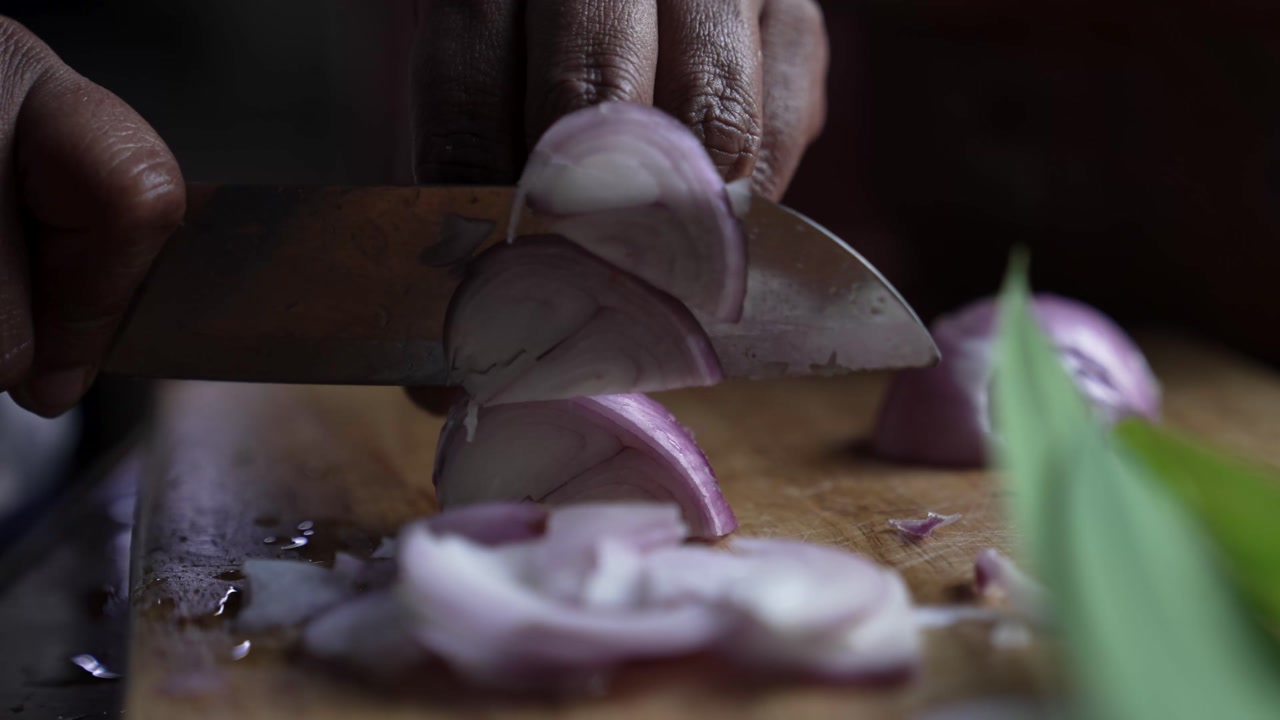 Close-up of onions being sliced during the preparation of a traditional Sri Lankan curry, capturing a key step in cooking.