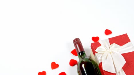 botella de vino, caja de regalo y corazones rojos dispersos en superficie blanca 4k
