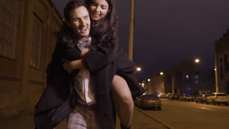 couple dressed in stylish clothes walking down the street celebrating new year, the guy carries the girl over his back