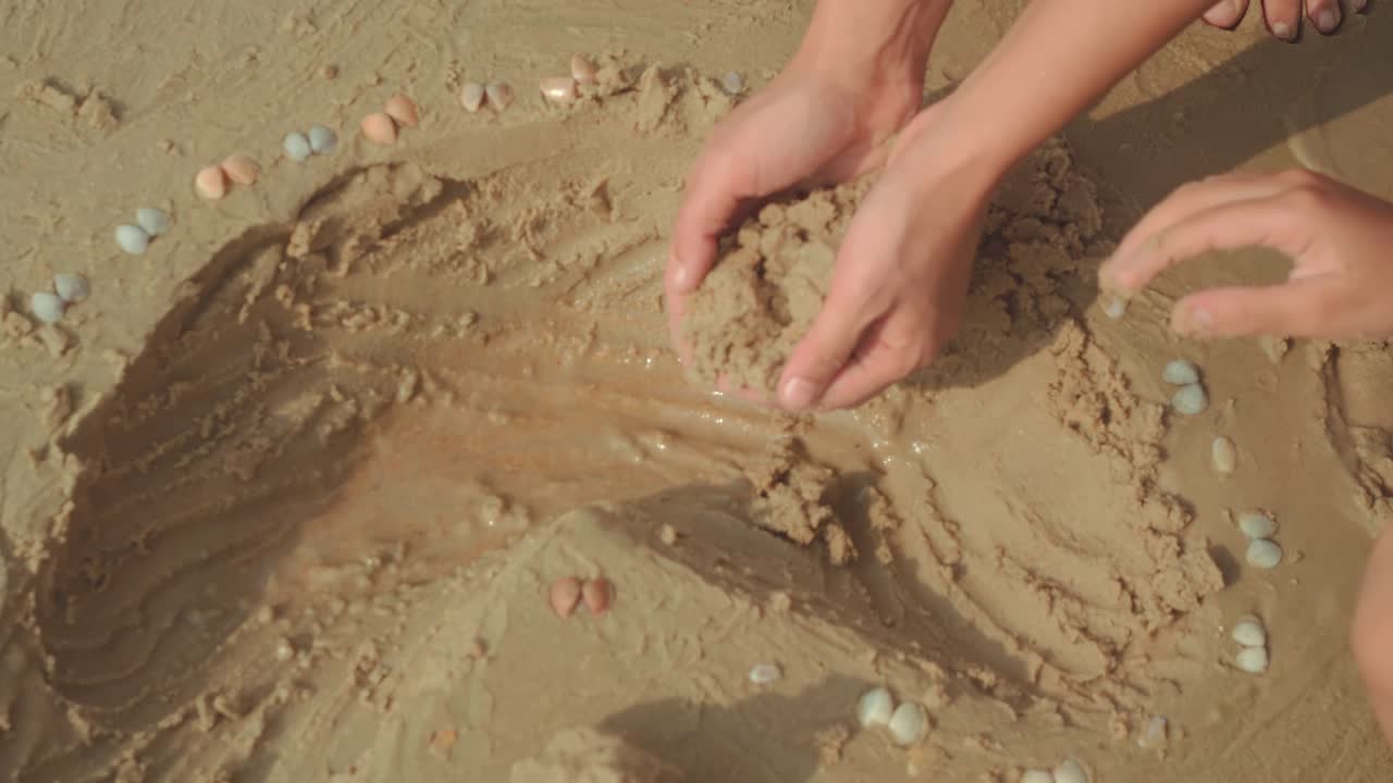 Närbild av händer som formar våt sand och vatten på stranden, en lekfull familjescen på sommaren.
