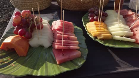 colorful arrangement of watermelon, melon, papaya, mango, and grapes, served on green leaf shaped platters, creating a visually appealing tropical fruit display