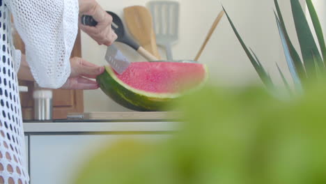 Nahaufnahme-Einer-Frau-In-Einem-Weißen-Kleid,-Die-In-Der-Küche-Mit-Einem-Großen-Messer-Eine-Reife-Wassermelone-Auf-Einem-Holzbrett-Schneidet