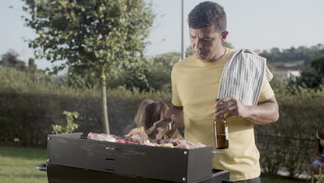 smiling man turning over meat on barbecue grill outdoors