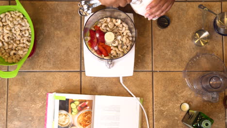 measuring teaspoons of salt into a food processor filled with roasted red peppers and cashews to make a delicious nutty dip or sauce - overhead view