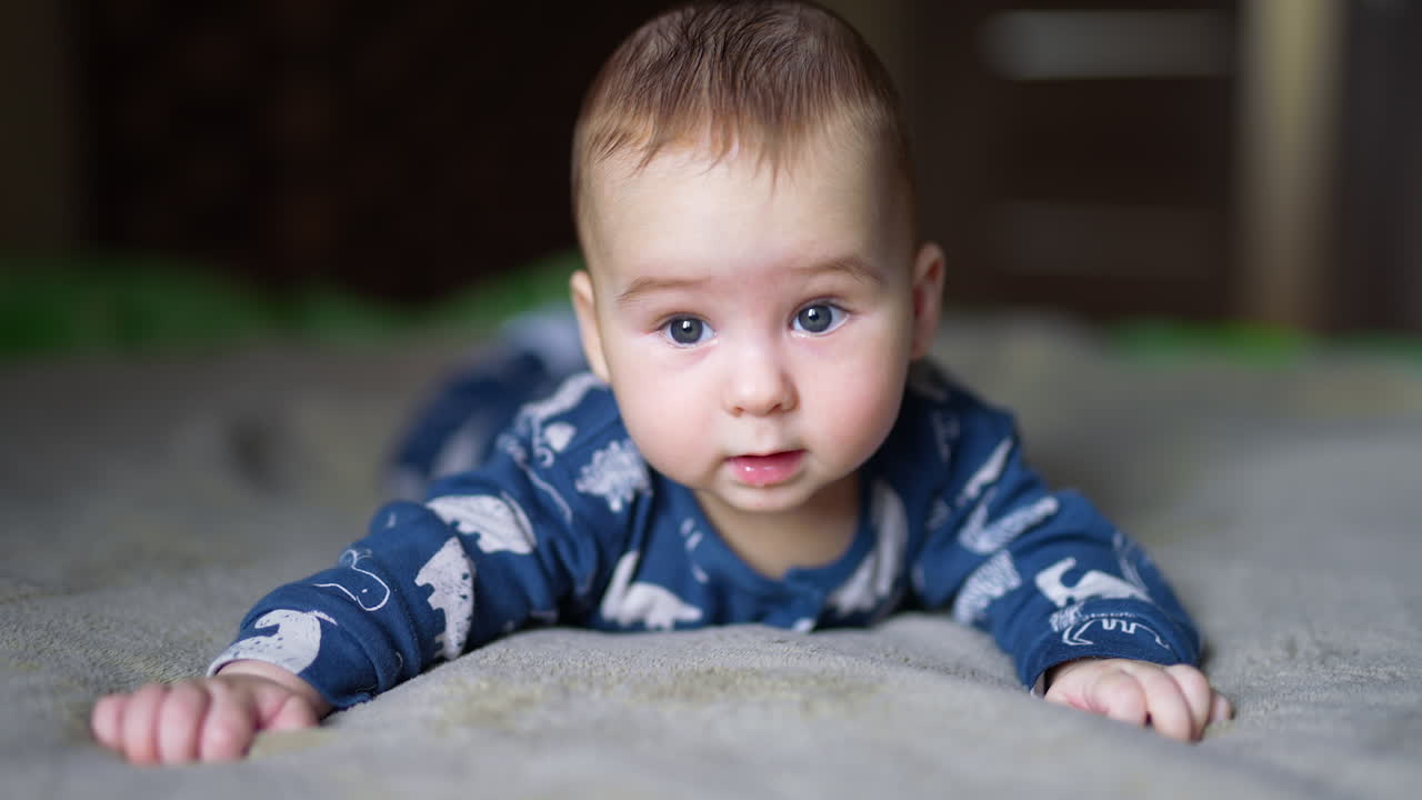 Beautiful child lies on belly keeping head steadily and looking around and down. Adorable kid close up.