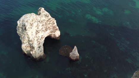 Tilting-up-to-view-calm-sea-and-limestone-cliffs-along-Algarve-coastline,-Portugal,-aerial