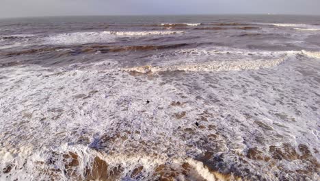 Vista-Aérea-De-Surfistas-Nadando-En-La-Playa-Con-Olas-De-Espuma-Blanca-En-Katwijk-Aan-Zee,-Países-Bajos