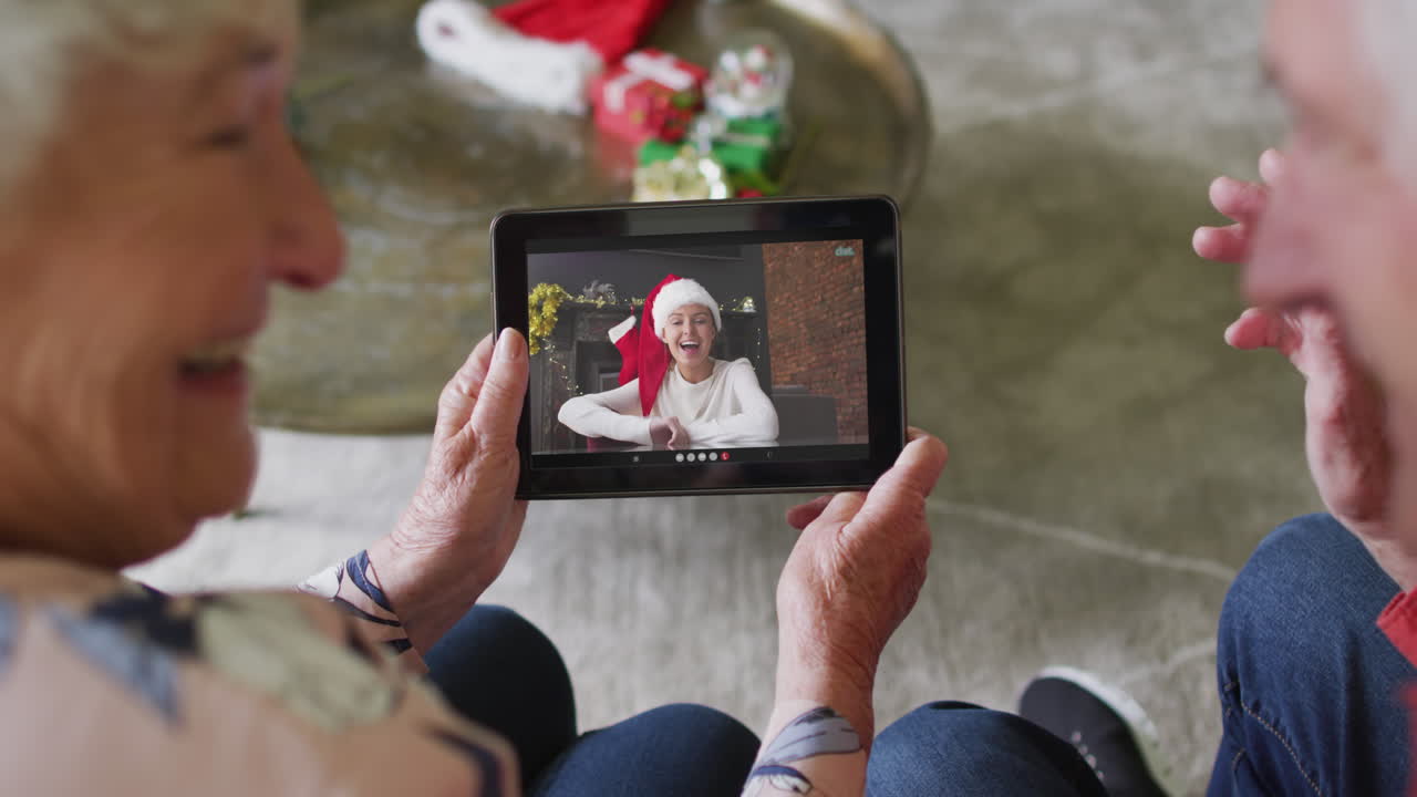 Coppia anziana caucasica sorridente che usa un tablet per una videochiamata di Natale con una donna sullo schermo