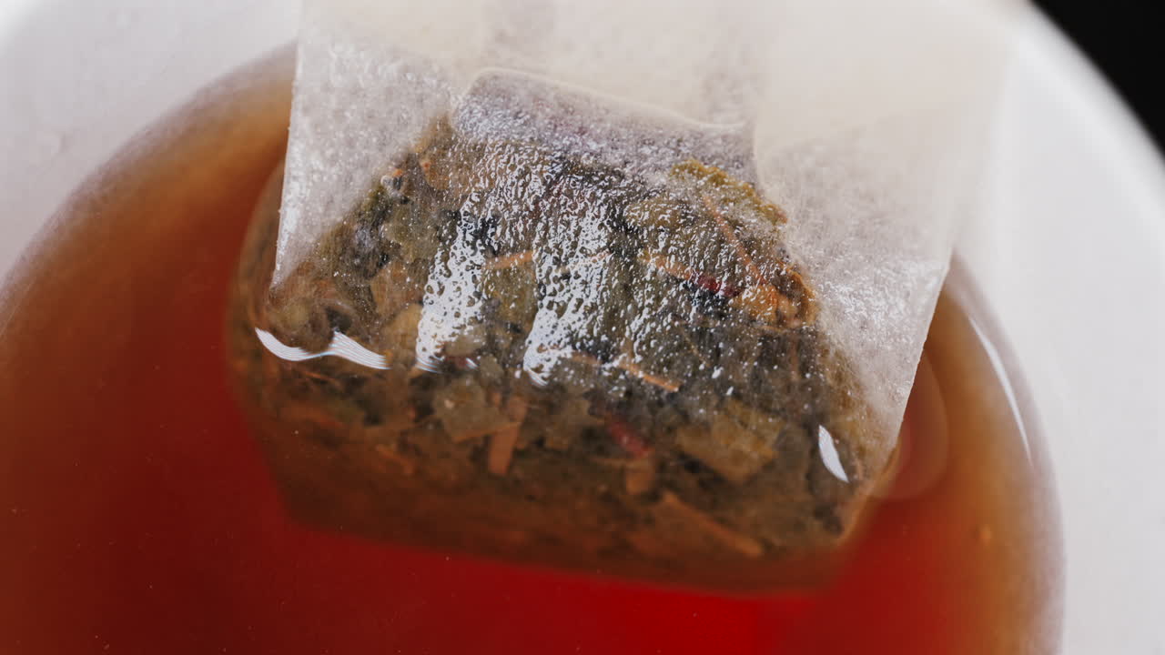 Close up of a tea bag steeping in hot water, releasing rich colour and aroma