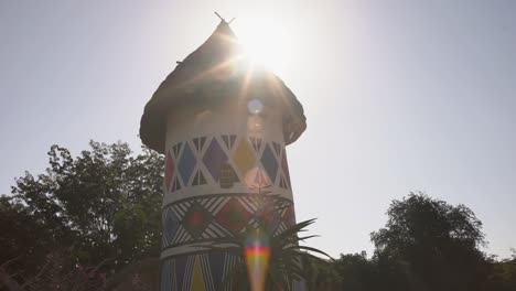 Moving-shot-of-Ndebele-patterns-on-hut-with-sun-moving-past-roof-in-the-background